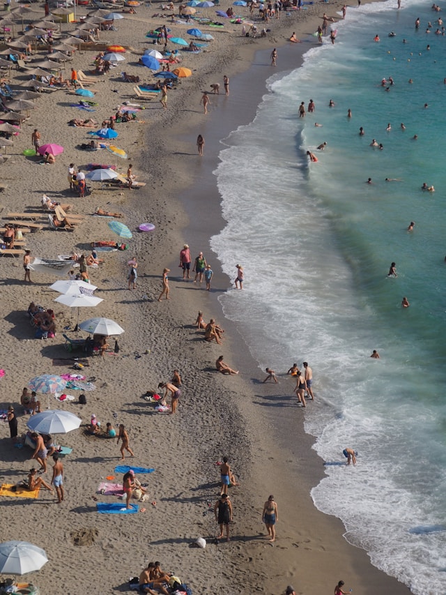 Visitors relaxing on beach chairs beside clear blue water.
